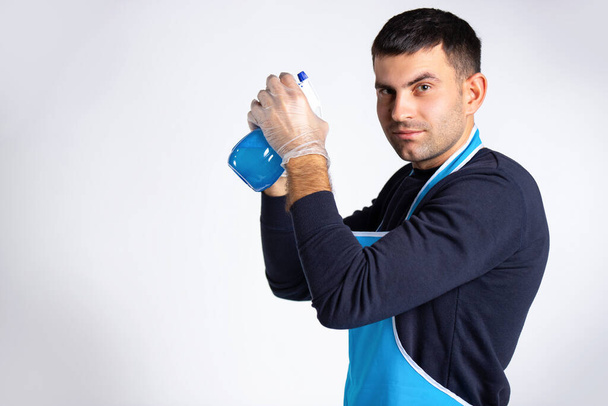 Concentrated man in rubber gloves with a spray in his hands looking at the camera. Gender equality concept. Photo on white background with empty side space. High quality photo - Foto, immagini