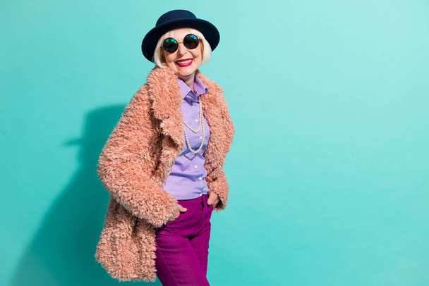 Photo of charming old woman dressed vintage outerwear cap eyewear smiling isolated turquoise color background - Foto, afbeelding