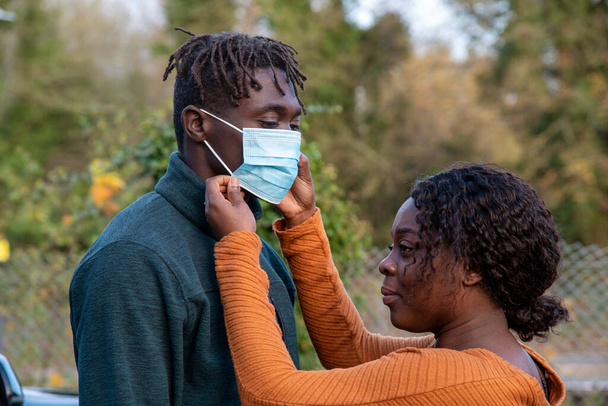 England, UK. 2020. Black couple with the woman adjusting her husbands facemask during Covid-19 outbreak. - Photo, Image