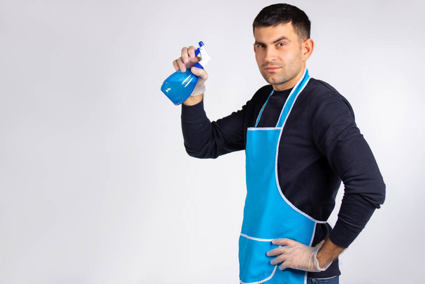 A pensive man in rubber gloves with a sanitizer in his hand looks into the camera. Gender equality concept. Photo over white background with empty side space. High quality photo - Photo, image