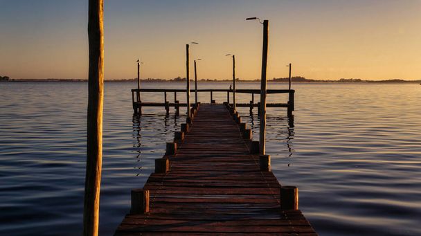 Puesta de sol en el lago Lobos, Buenos Aires. Tomado de la orilla mirando a un viejo muelle de madera grande y el lago                                - Foto, Imagen