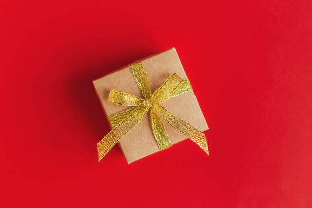 Gift box with golden ribbon on a red background with gold glitter. Place for text. Flat lay. - Фото, изображение