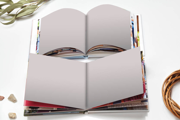 Zwei offene hochwertige Fotobücher mit gebundenen und leeren Seiten, grünem Zweig und kleinen Steinen isoliert auf weißem Studiohintergrund. Nahaufnahme, Kopierraum - Foto, Bild