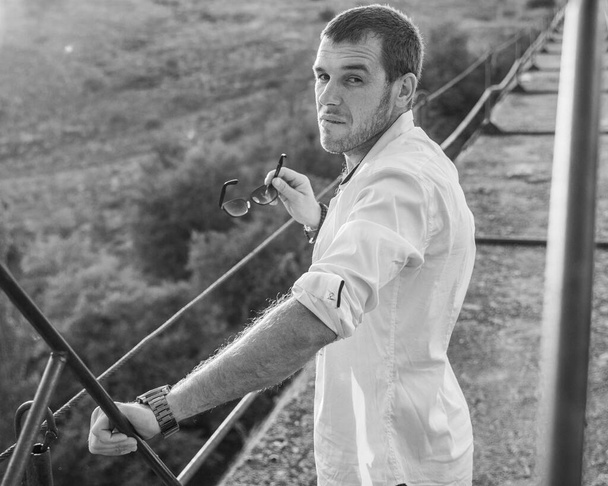 Noir et blanc Portrait d'un jeune homme séduisant dans une chemise blanche déboutonnée debout sur les marches de pierre de la vieille construction ourdoor - Photo, image