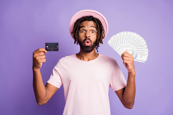 Photo of young african shocked amazed handsome guy male man wear glasses hold credit card dollars isolated on violet color background - 写真・画像