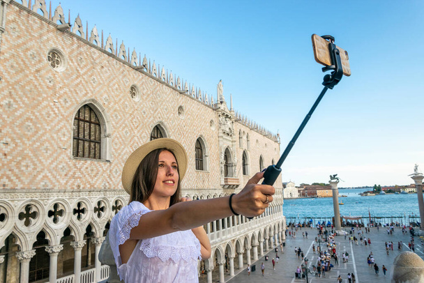 Mooie vrouw maakt leuke zelfportretfoto op San Marco plein in reizen Europa stad Italië, Venetië. Panoramisch uitzicht op de oude Italiaanse architectuur met historische brug, romantische boot. Venetië - Foto, afbeelding