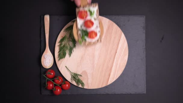 Crispbread with creamy cheese, cherry tomato fresh herbs on a black background. from the top. flat lay. - Footage, Video
