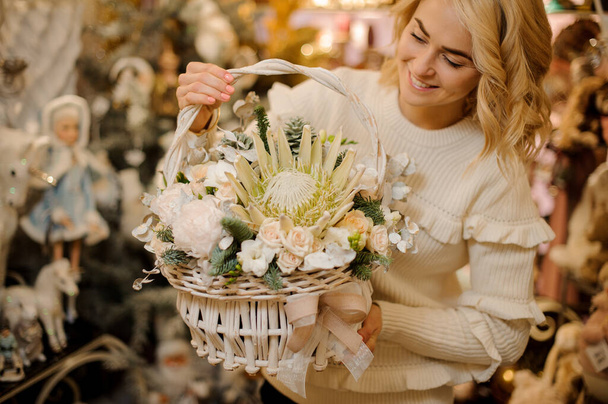 awesome floral arrangement of flowers and spruce branches in white wicker basket in hands of pretty woman - Photo, Image
