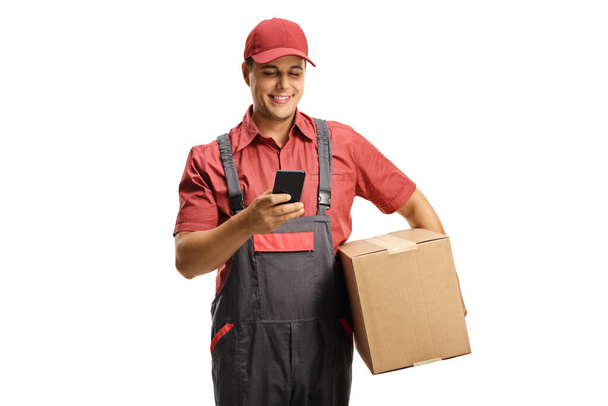 Male courier in a uniform holding a box and typing on a mobile phone isolated on white background - Valokuva, kuva