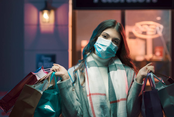 Woman shopping during coronavirus pandemic, she is wearing a surgical mask and holding shopping bags - Photo, image