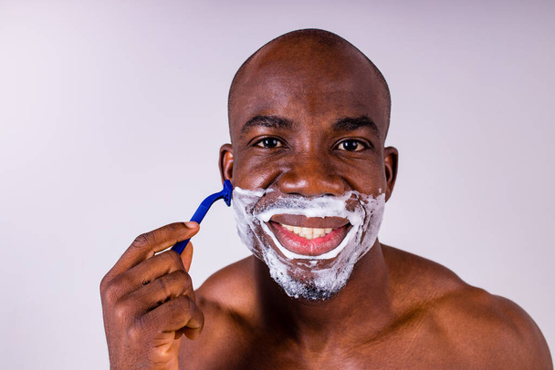 latin hispanic man with razor and shaving foam on his face studio white isolate background - Fotó, kép