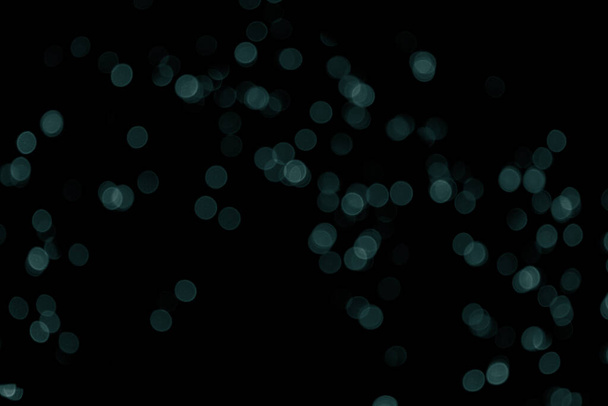 Defocused bokeh christmas small green lights on black background. Blurred abstract green glitter texture. Dark green bokeh glitter wallpaper for Christmas, New year or festival background. Tidewater Green colors. - Photo, Image