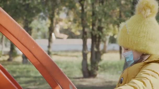 Маленька дівчинка на медичній захисній масці на обличчі грає на дитячому майданчику в міському парку
 - Кадри, відео