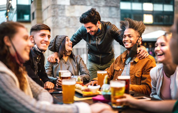Jovens bebendo cerveja com máscara de rosto aberto - Novo conceito de estilo de vida normal com milenial se divertindo juntos conversando em happy hour no bar da cervejaria externa - Filtro quente com foco em pessoas centrais - Foto, Imagem