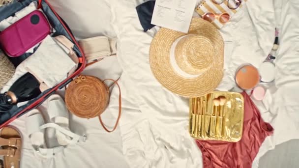 Von oben flache Mütze, Sonnenbrille, Badeanzug und halb gepackter Koffer auf dem Bett liegend - Filmmaterial, Video