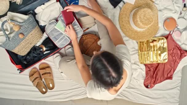 Pohled shora zvětšit záběr mladé ženy sedící na posteli a balící na výlet. Dává pas a letenky do pořadače dokumentů, který leží v jejím kufříku. - Záběry, video
