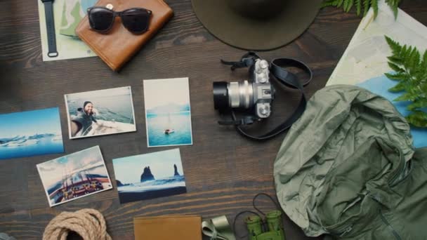 PAN bovenaanzicht van reisspullen, fotocamera, lantaarn, varen en foto 's van recente reizen liggend op houten tafel - Video