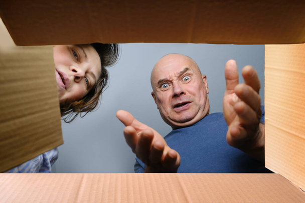 woman and a man opened a cardboard box with an ordered product, look into it, emotionally reacts to the contents, the concept of a postal item, a package, buying goods online - Foto, imagen