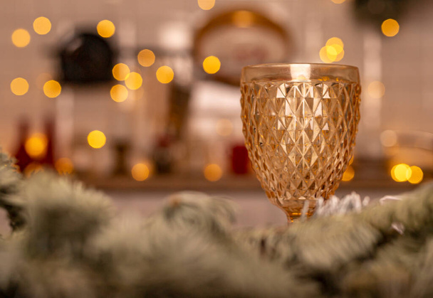 Yellow glass for wine ove blurred background of kitchen decorated for christmas with lights. - Фото, изображение