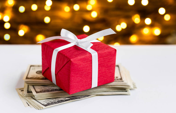 Red gift box on the USA 100 dollar bills on blurred lights background. American dollar. Christmas and New Year money present. Gift cost. Hundred. Finance and business concept. Christmas shopping - Valokuva, kuva