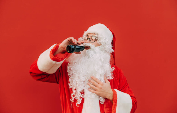 Ο Άγιος Βασίλης κλείνει τα μάτια του στην απόλαυση ενώ πίνει γλυκό αναψυκτικό κόλα. Γενειοφόρος Άγιος Βασίλης αισθάνεται ευχαρίστηση ακόμα κι αν έχουν ανθυγιεινή διατροφή. - Φωτογραφία, εικόνα