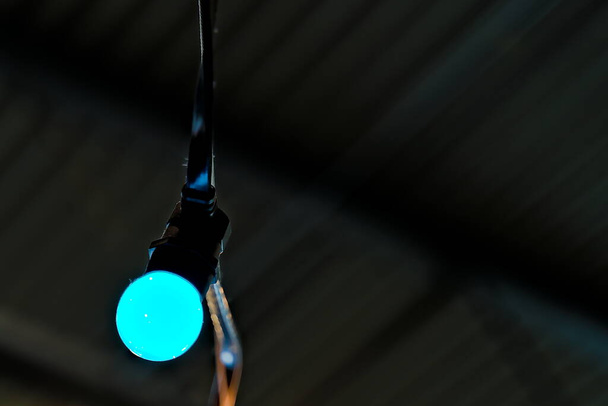 Single blue party light bulb suspended from ceiling.  - Photo, Image