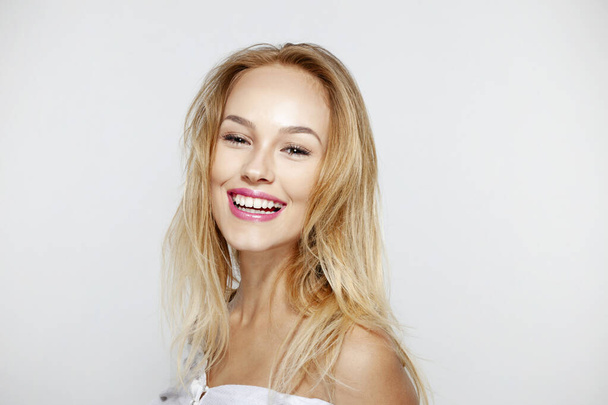Mujer joven rubia feliz con hermoso maquillaje natural y largo cabello ondulado, con hombros desnudos, sobre fondo blanco. - Foto, imagen