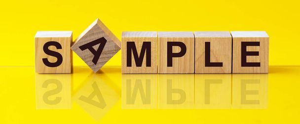 SAMPLE - słowo wykonane z drewnianych klocków koncepcji, żółte tło. - Zdjęcie, obraz