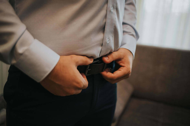 a man with a gray shirt and black pants wearing his belt - Fotoğraf, Görsel