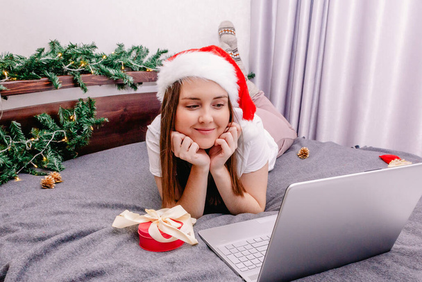 a young happy brunette wishes her family and friends a happy new year and Christmas over the Internet using a laptop. - Фото, зображення