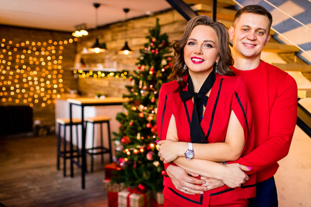 Good-looking, attractive brunette lady in red dress with her man in cozy living room with lights garland decorations - Foto, afbeelding