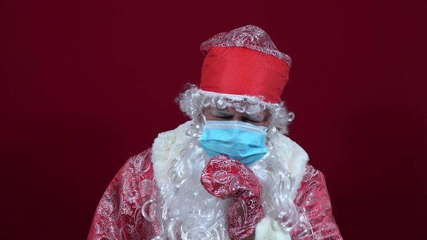 Russian santa claus in a medical mask on a red background sits sad without gifts 4k - Foto, Imagem
