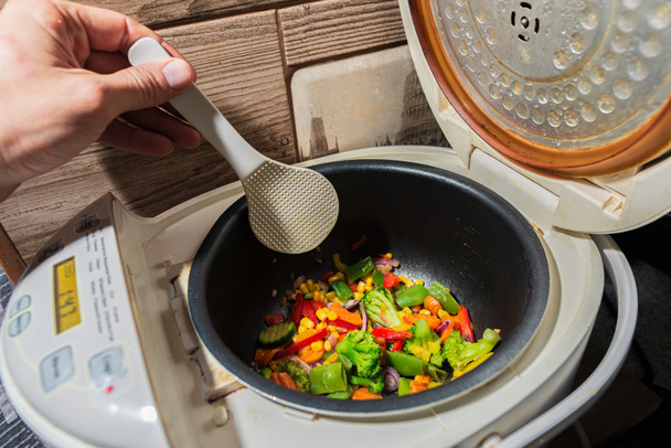 Farklı sebzelerden oluşan karışık bir mutfak plastik kazıyıcıyla karıştırılır. Soğan, biber, biber, bezelye, mısır, brokoli, lahana ve salatalık. - Fotoğraf, Görsel