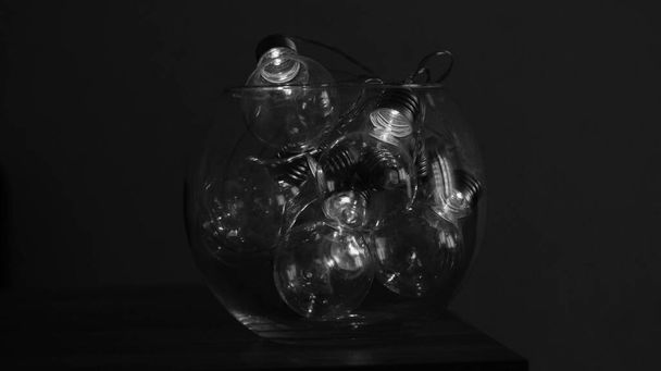 Guirlandes électriques sous la forme d'une ampoule en boule transparente briller dans le noir et blanc foncé - Photo, image