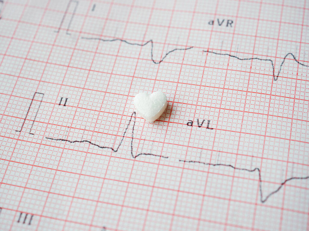 Compressa bianca a forma di cuore su carta ECG risulta come sfondo. Pillola cardiologica medica a forma di cuore. Il farmaco per ripristinare la salute. Concetto medico e sanitario. - Foto, immagini