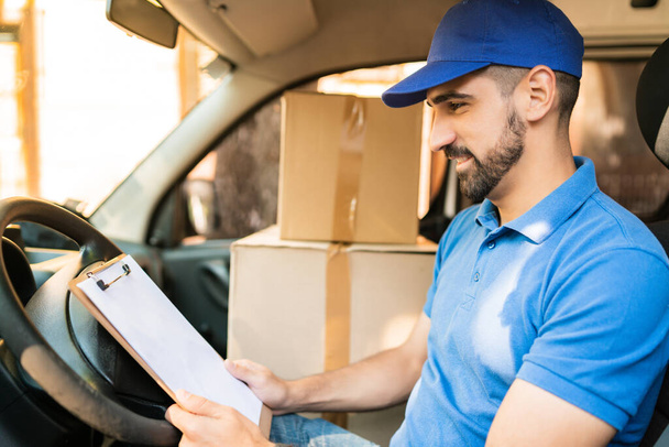 Delivery man checking delivery list in van. - Foto, Bild