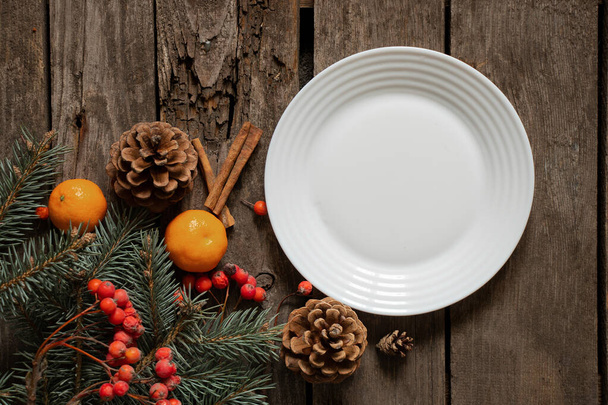 dennentak en viburnum mandarijnen kaneel en wit leeg bord op tafel, nieuwjaarsdecor op tafel tijdens de feestdagen - Foto, afbeelding