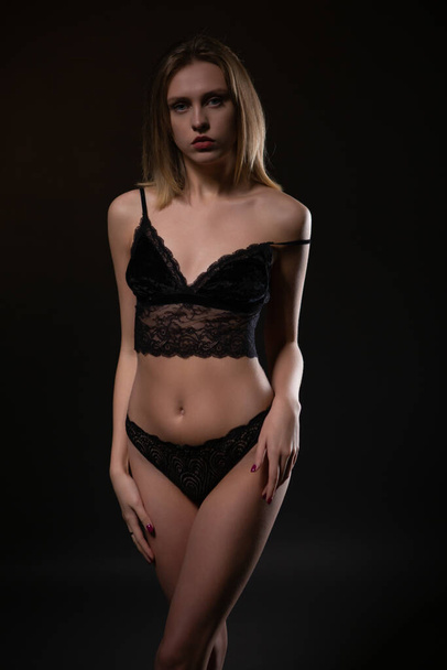 Young beautiful woman posing in black lace underwear on dark background - Photo, image