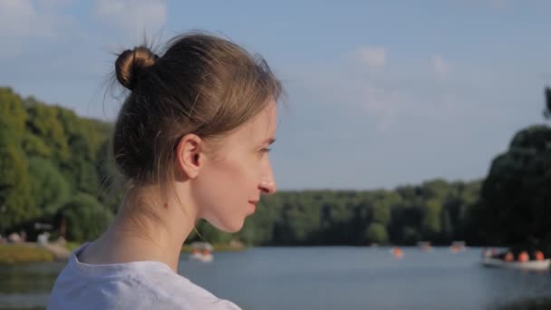 Jovem mulher de camisa branca sentada e olhando para lagoa - câmera lenta - Filmagem, Vídeo