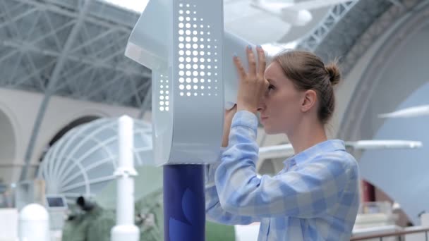 Молодая женщина смотрит в белый телескоп и исследует выставку - Кадры, видео