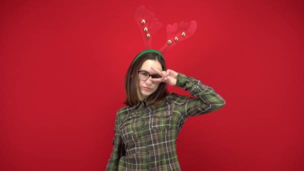 Een jonge vrouw danst met een hoofdband in de vorm van een kerstgewei. Studio schieten op een rode achtergrond. - Video