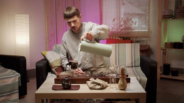 A young man prepares for a romantic date with an authentic japanese tea ceremony at home, pours boiling water into a teapot with an infuser. - 写真・画像