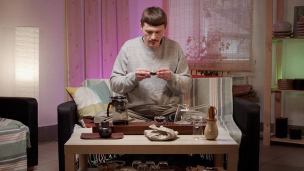 Un hombre se relaja en casa en auto-aislamiento con la ayuda de una ceremonia del té chino. Medita y bebe té chino calmante antes de ir a la cama. - Foto, Imagen