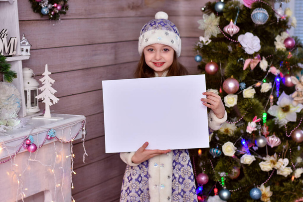 A girl in a Santa Claus helper costume. The girl holding blank piece of paper and pointing to copy space. - Photo, Image