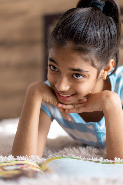 childhood, emotions, solitude, beauty concept - portrait of happy young minor cheerful joyful dark-skinned girl of middle eastern persian appearance 6-9 years old smiling cutely lying on bed indoors. - Foto, afbeelding
