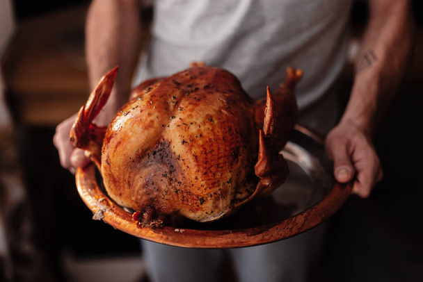 Man holds roasted turkey on a metal cooper round tray. Festive poultry dish. Holiday season Thanksgiving Day, Christmas dinner. Family holiday celebration. Autumn end of November, Thursday. Harvest - Фото, зображення