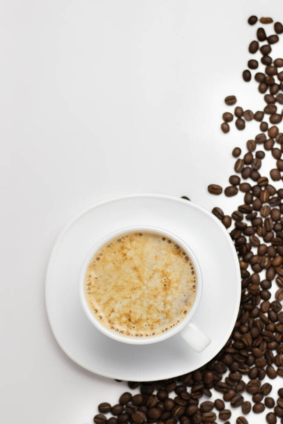 Fondo blanco limpio desde arriba con una taza y platillo lleno de café y granos de café esparcidos en la esquina. - Foto, Imagen