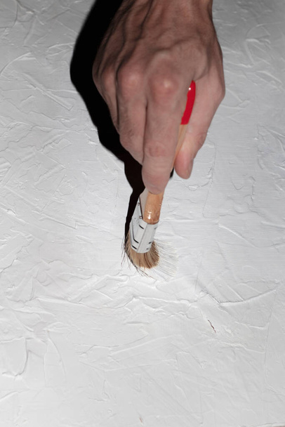 Macun ve boyadan beyaz beton bir arkaplan oluşturma süreci. Beyaz bir adamın eli küçük bir fırça tutuyor ve macunu boyuyor.. - Fotoğraf, Görsel