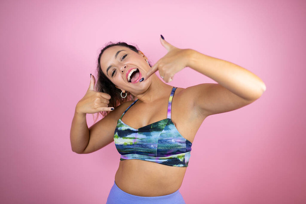 Young beautiful woman wearing sportswear over isolated pink background doing the call me gesture with her hands - Zdjęcie, obraz
