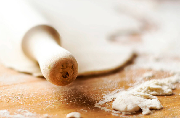 Wooden rolling pin on a wooden surface with some flour and a dough. Preparation of baked food - Foto, Bild